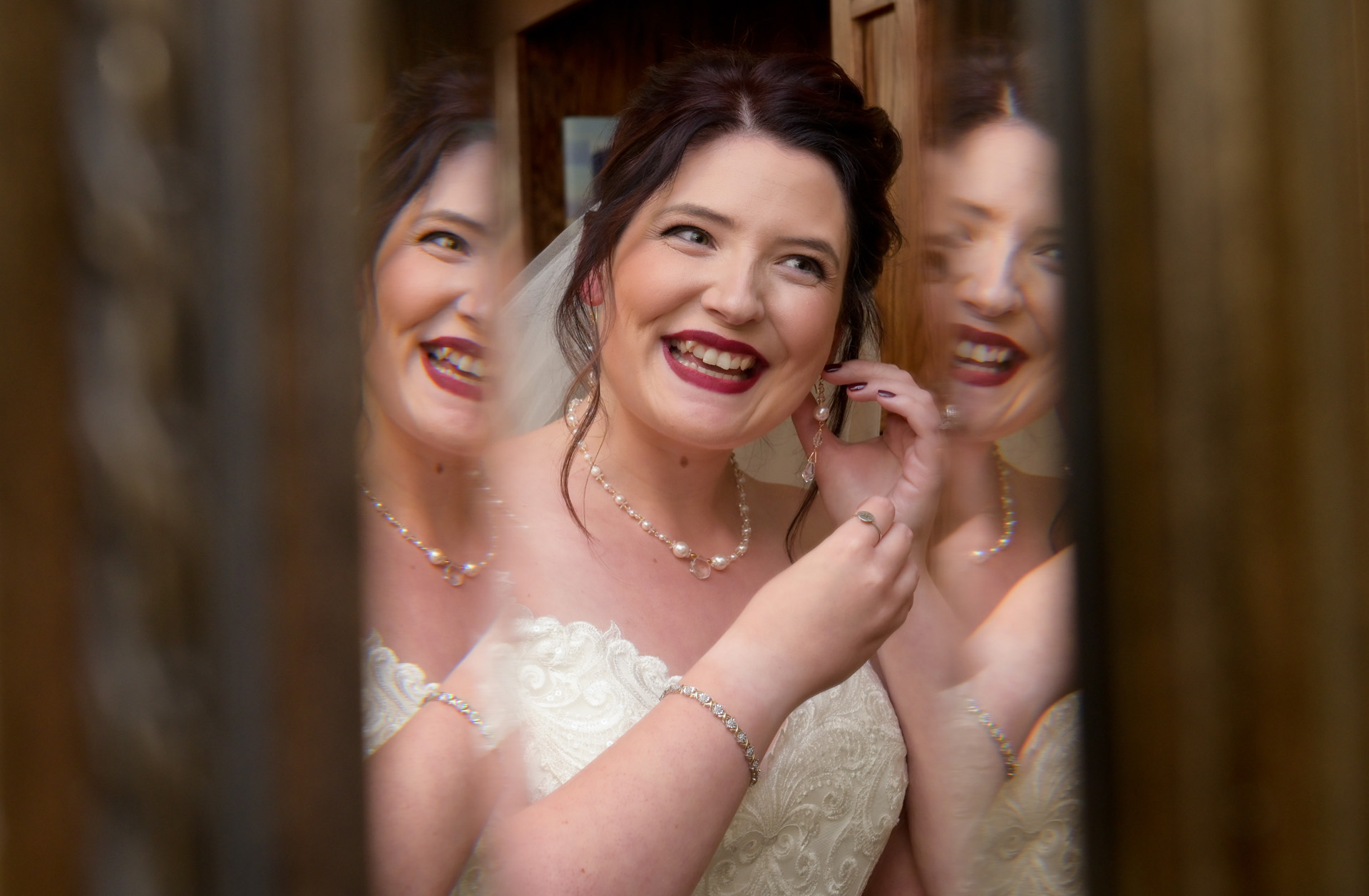 A bride grins while putting in her earrings before her wedding in Livonia, Michigan. I love how she's refracted in the mirror.