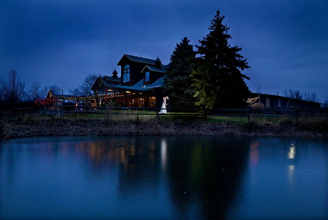 The bride and groom pose for this wedding photo at dusk for their winter wedding at the Fenton Brewery in Fenton, Michigan.
