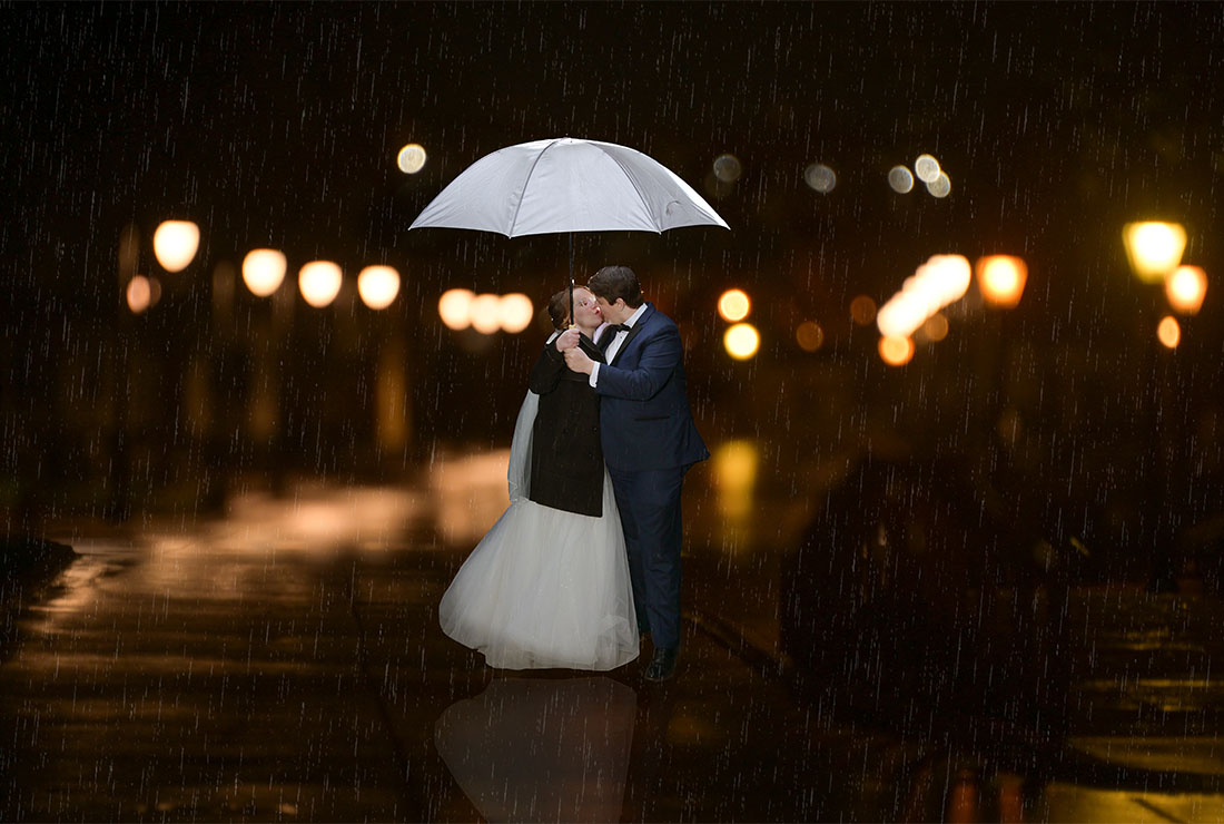 The The bride and groom smooch under an umbrella after dodging rain drops all wedding day long at the Henry Ford Museum in Dearborn, Michigan.