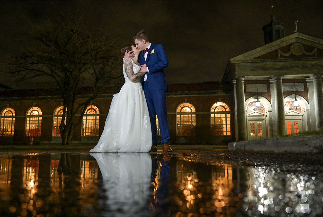 The bride and groom cuddle outside reflecting in a puddle after dodging rain all day after their wedding at Lovett Hall at the Henry Ford Museum in Detroit, Michigan.