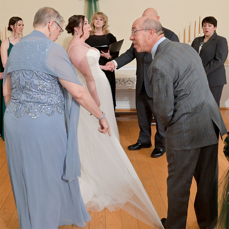 The father of the bride steps on his daughter's dress during the wedding at Mills Race Historical Village in Northville, Michigan.