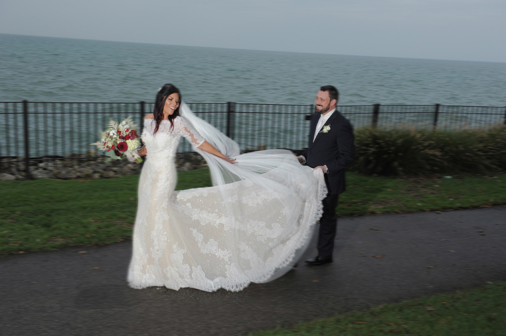 A Grosse Pointe, Michigan groom holds his bride's wedding dress train during their wedding at Pier Park in Grosse Pointe Michigan.