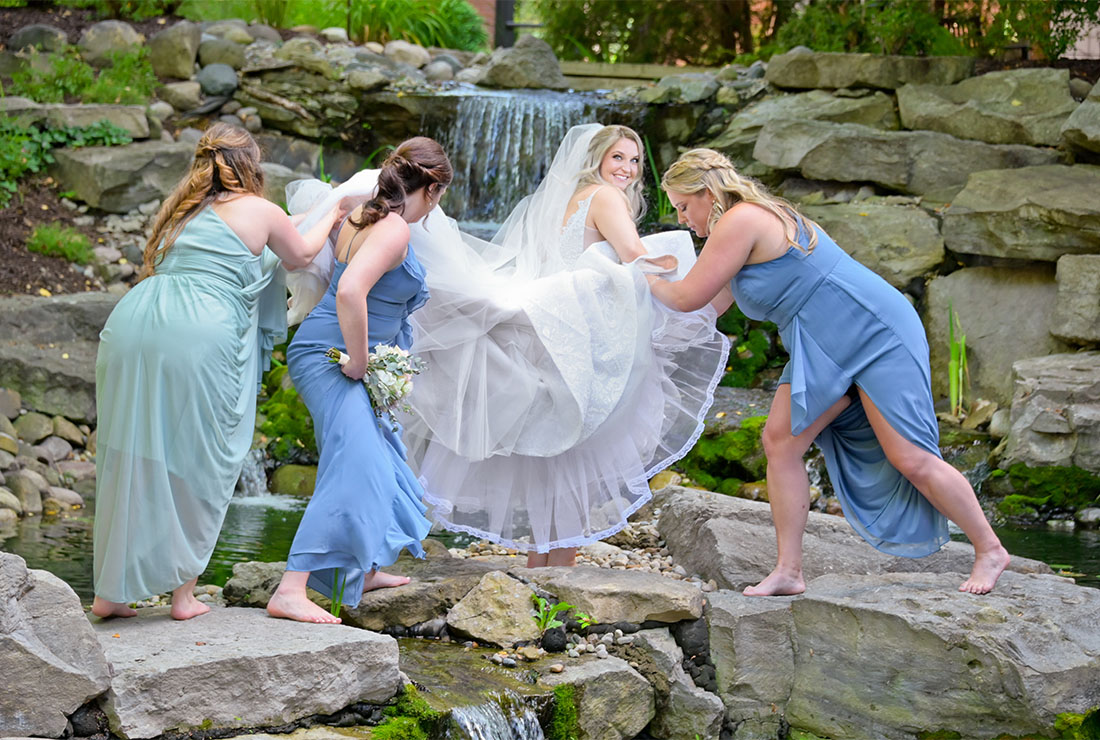 Wedding party members help the bride over rocks before her wedding at at St. Johns Resort in Plymouth, Michigan