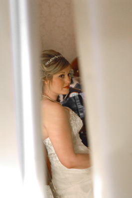 The bride peeks from behind a curtain separating her from the groom at her Troy MI wedding