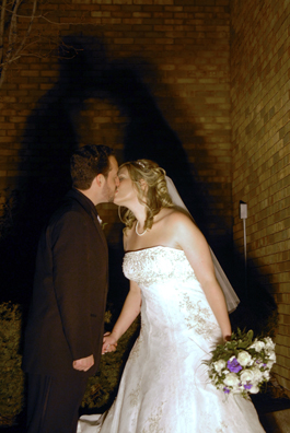 The bride and groom kiss outside under funky lights at their Troy, Michigan reception Hall