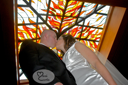 The bride and groom kiss under the stain glass at their Catholic church in Macomb Michigan