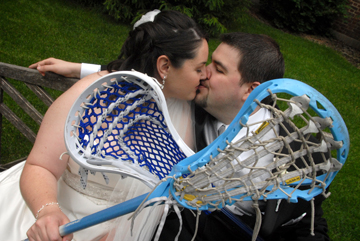 =bride and groom kiss under the cross of lacrosse sticks at their Henry Ford Museum wedding in Dearborn, Mi