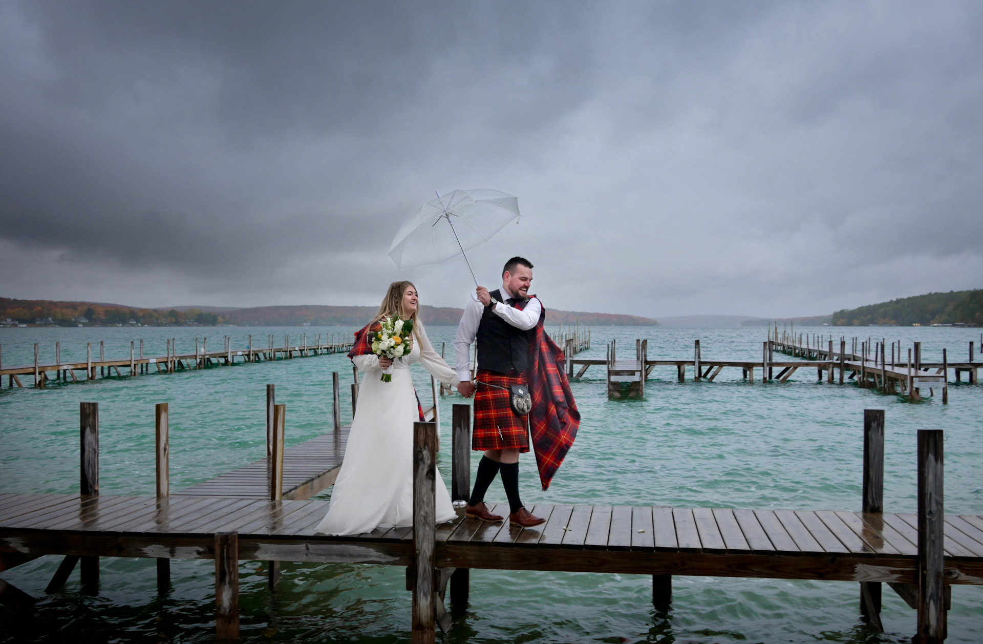 The groom sort of tries to keep his bride dry during their wet destination in Northern Michigan on Walloon Lake during a soggy fall wedding.