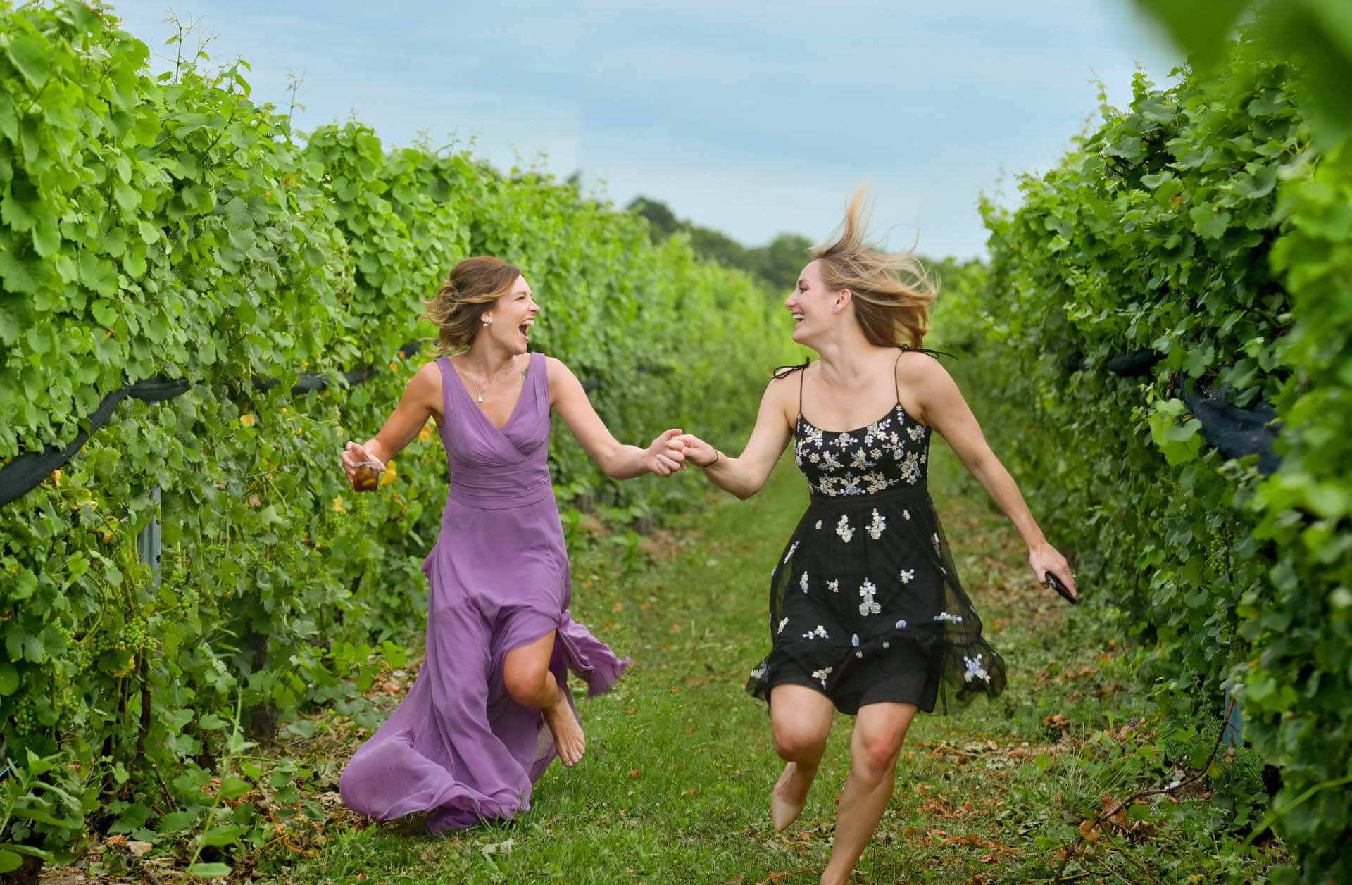 Two wedding guests run through a vineyard after a destination wedding in Traverse City, Michigan for this fun wedding photo.