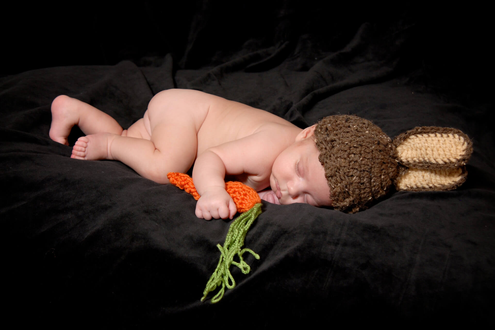 Best Detroit baby photographer's  newborn photos of a newborn baby with a rabbit hat and a carrot during the photography session in her studio in Troy, Michigan area.
