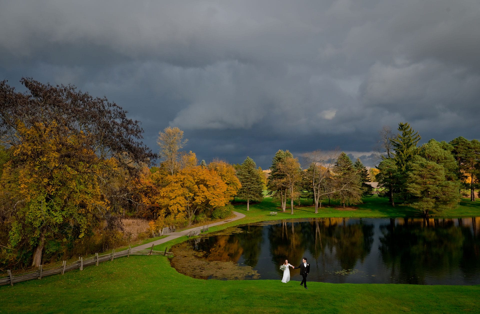 Bride and groom head away from the pond before a storm hits at Addison Oaks Buhl Estate in Leonard, Michigan.