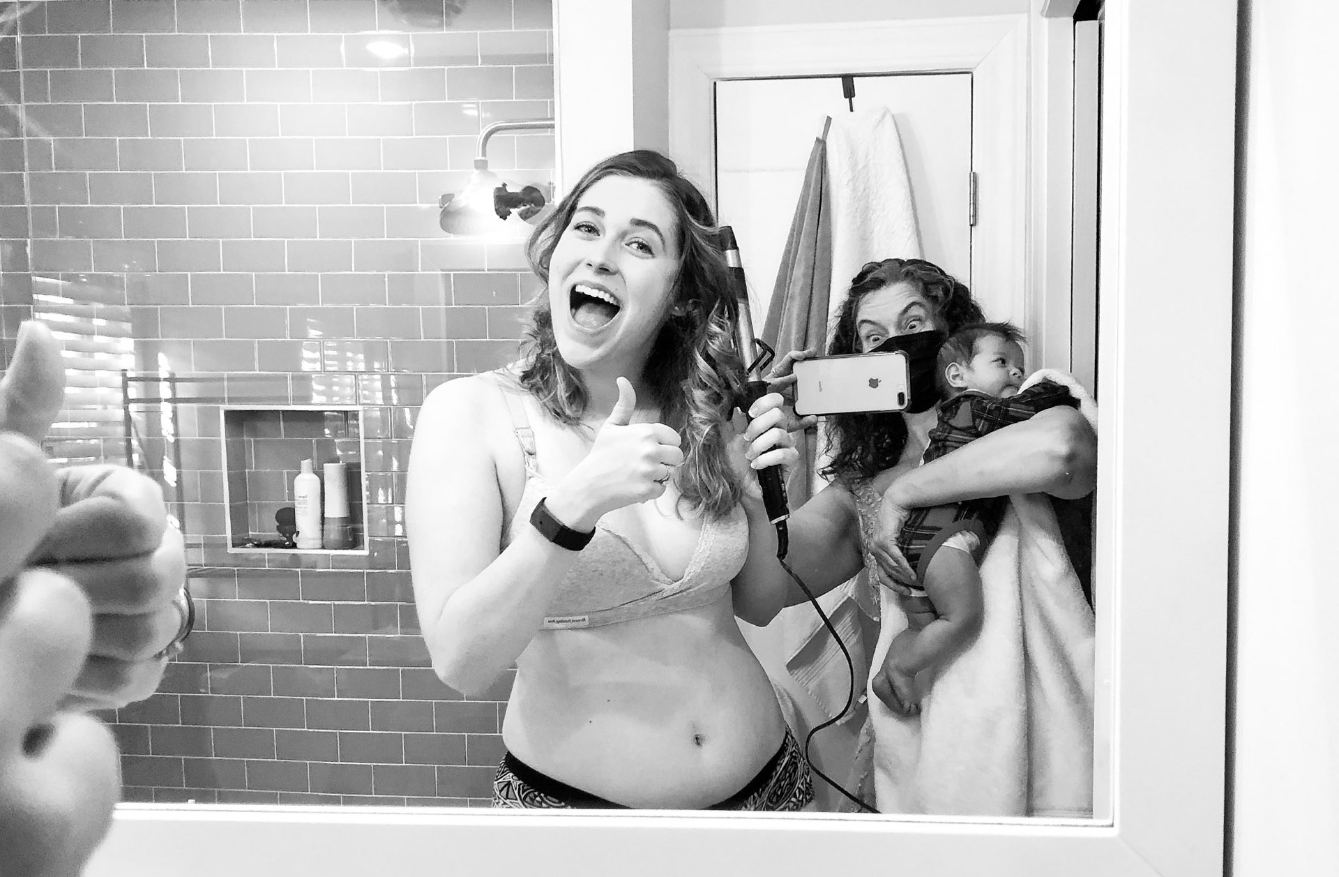 The maid of honor gets ready in the bathroom while the mother of the bride tries to take photos while also babysitting.