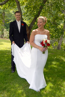 The groom helps the bride hitch up her dress after the ceremony in Midland MIchigan